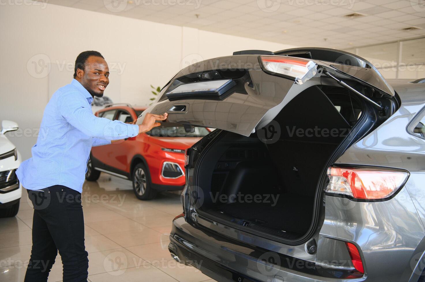 feliz carro comprador, Novo carro proprietário conceito. retrato do animado jovem africano americano cara dentro concessionária sala de exposições foto