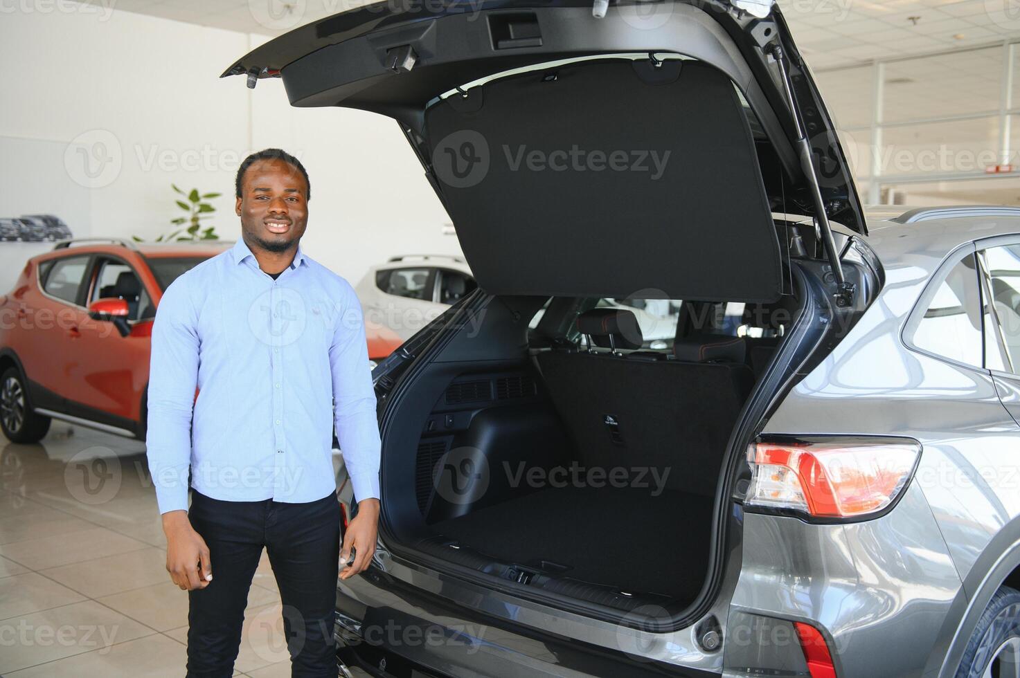 feliz carro comprador, Novo carro proprietário conceito. retrato do animado jovem africano americano cara dentro concessionária sala de exposições foto