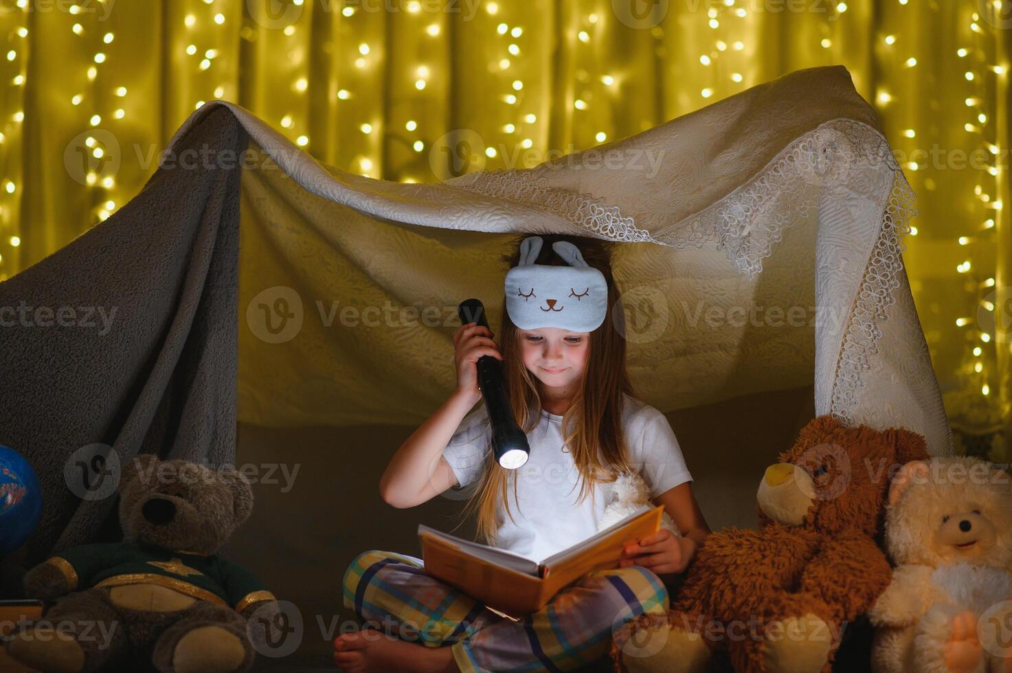 criança menina lendo com livro e lanterna e Urso de pelúcia Urso dentro barraca. antes indo para cama. foto