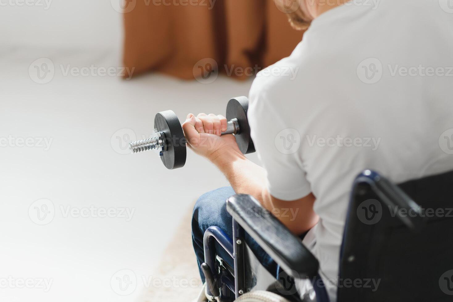 desportista sentado dentro cadeira de rodas e estendendo-se braços com halteres durante reabilitação exercício dentro moderno médico Centro. foto