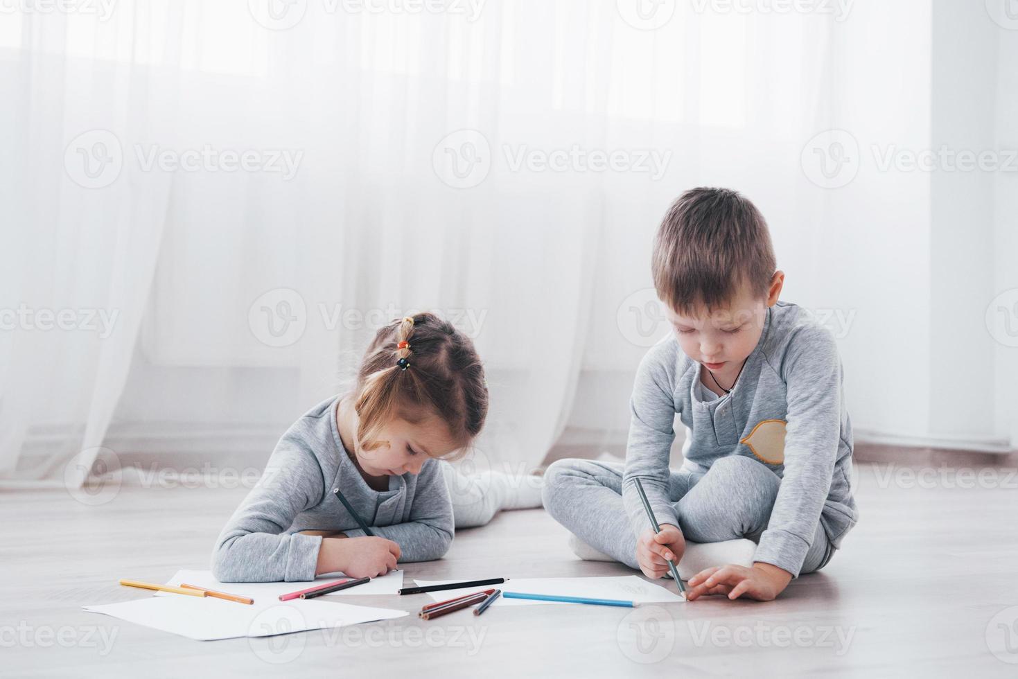 crianças deitam-se no chão de pijama e desenham a lápis. criança fofa pintando a lápis foto