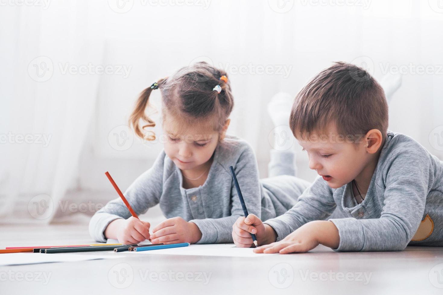 crianças deitam-se no chão de pijama e desenham a lápis. criança fofa pintando a lápis foto