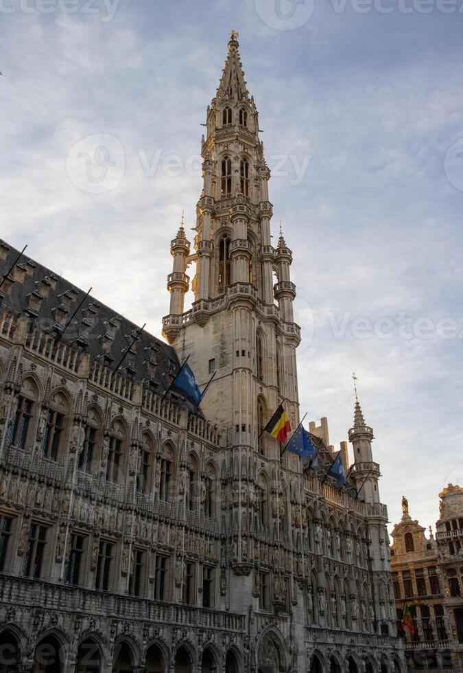 icônico pináculo do a Bruxelas Cidade corredor debaixo uma nublado céu, adornado com Belga e eu bandeiras - uma gótico maravilha foto