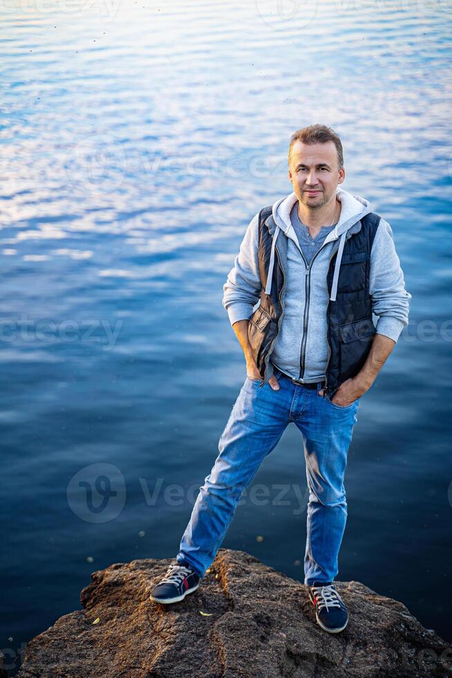 homem contemplando a sereno beleza do natureza. uma homem em pé em topo do uma Rocha Próximo para uma corpo do água foto