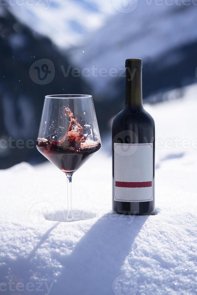 uma garrafa do vermelho vinho e uma vidro do vinho sentado em uma Nevado terra foto