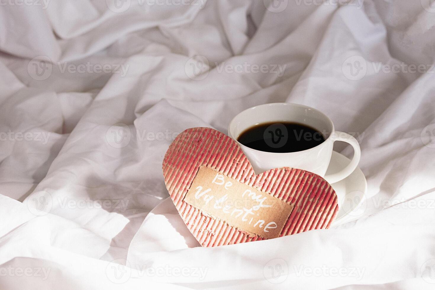festivo dia dos namorados manhã dentro cama. feito à mão namorados cartão e café copo em amarrotado roupa de cama. foto