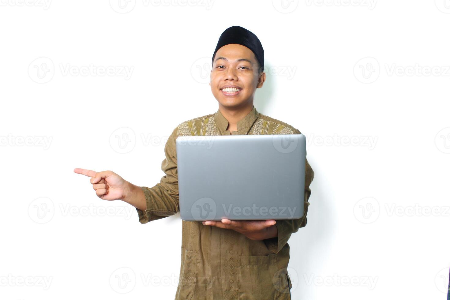 sorridente ásia muçulmano homem segurando computador portátil apontando para ao lado isolado em branco fundo foto