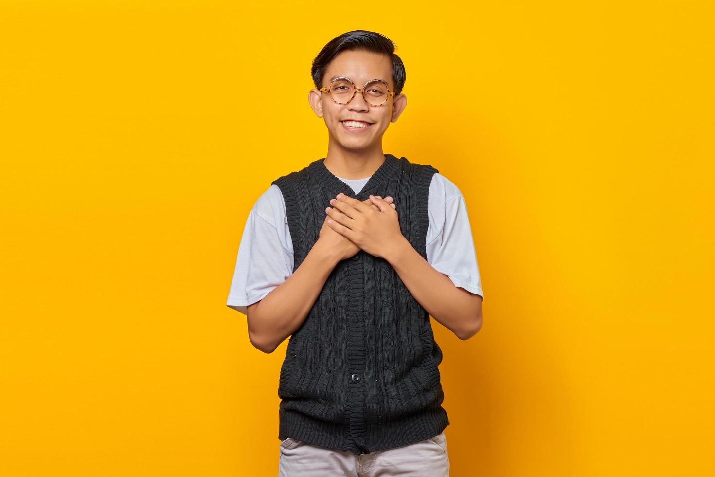 felicidade, jovem asiático, mantendo as duas palmas das mãos no peito isoladas sobre fundo amarelo foto