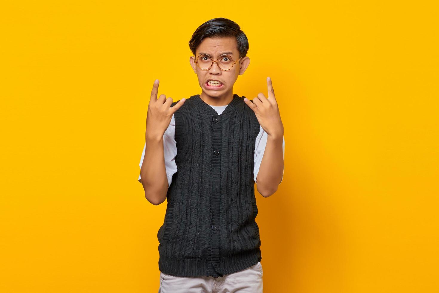 retrato de jovem asiático vestindo roupas casuais, gritando com uma expressão maluca fazendo o símbolo do rock com as mãos para cima foto