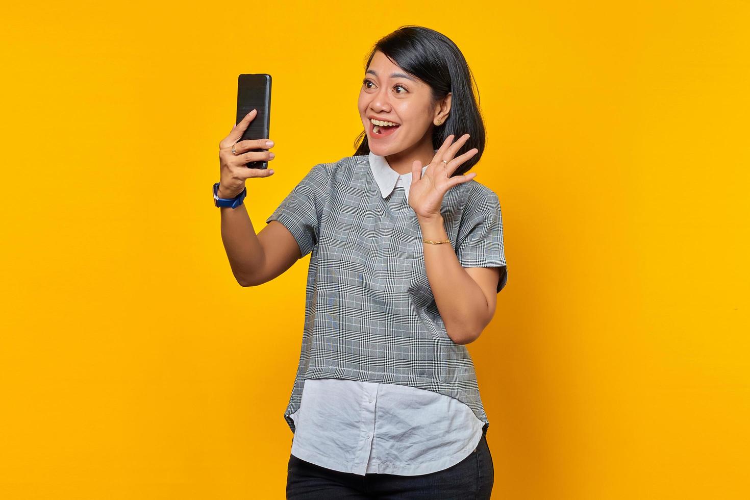 retrato de mulher asiática jovem e animada usando telefone celular, tirar selfie sobre fundo amarelo foto