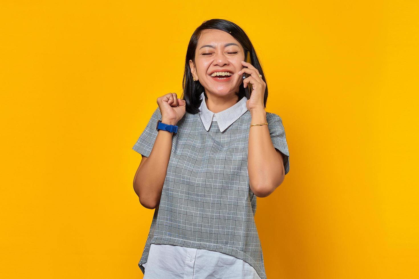 alegre jovem asiática recebendo uma chamada no smartphone e olhando para o lado no fundo amarelo foto