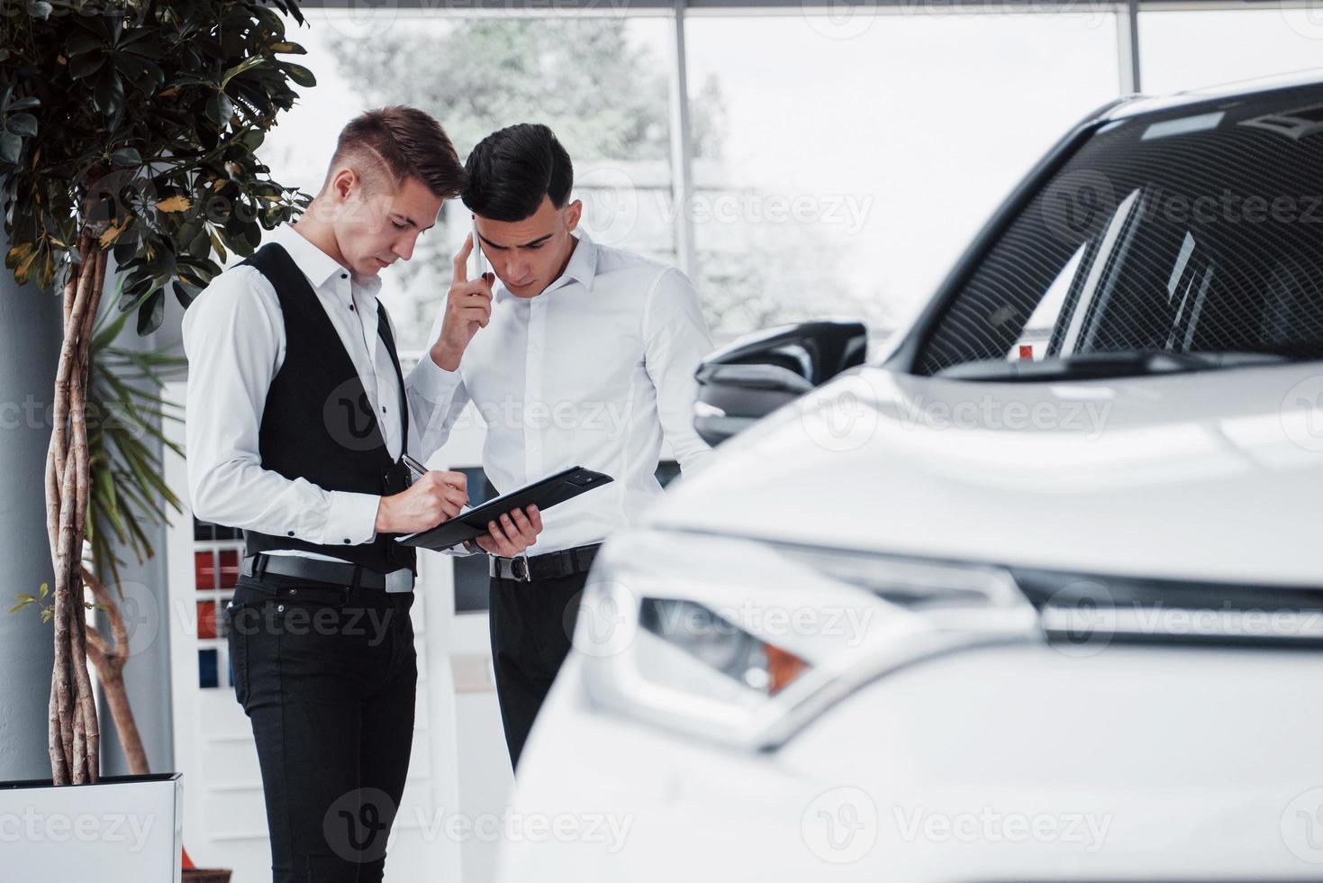 dois homens estão no showroom contra carros. close-up de um gerente de vendas em um terno que vende um carro para um cliente. o vendedor dá a chave ao cliente. foto