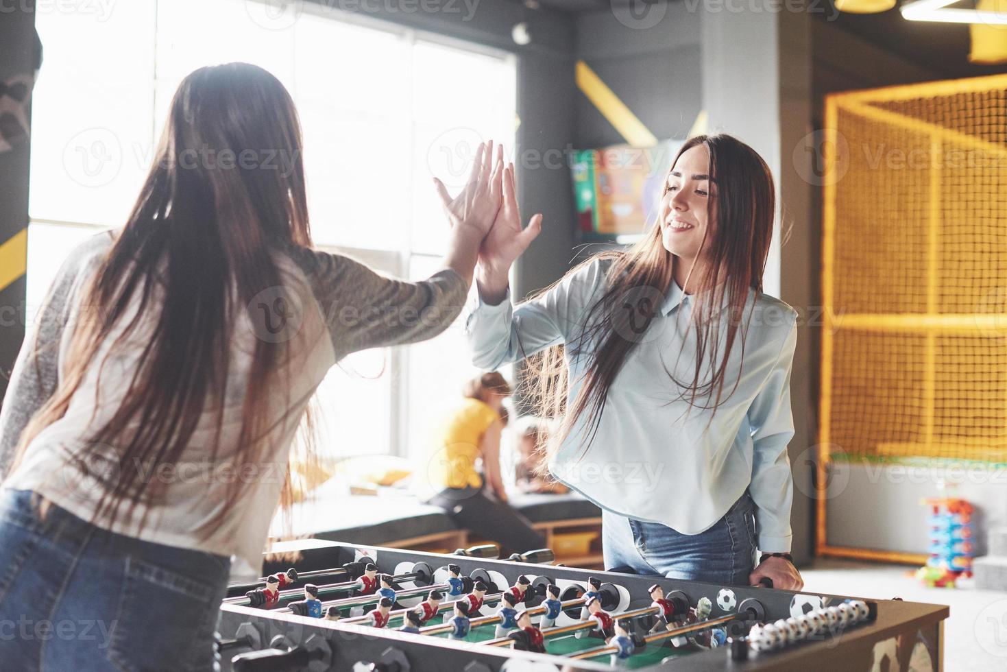 duas lindas gêmeas jogam futebol de mesa e se divertem. uma das irmãs segura uma bola de brinquedo na mão e mostra a língua foto