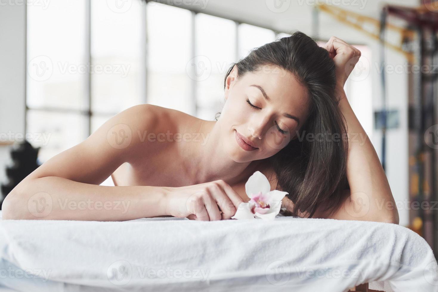 uma bela jovem relaxando com uma flor de orquídea, em frente a uma massagem. foto