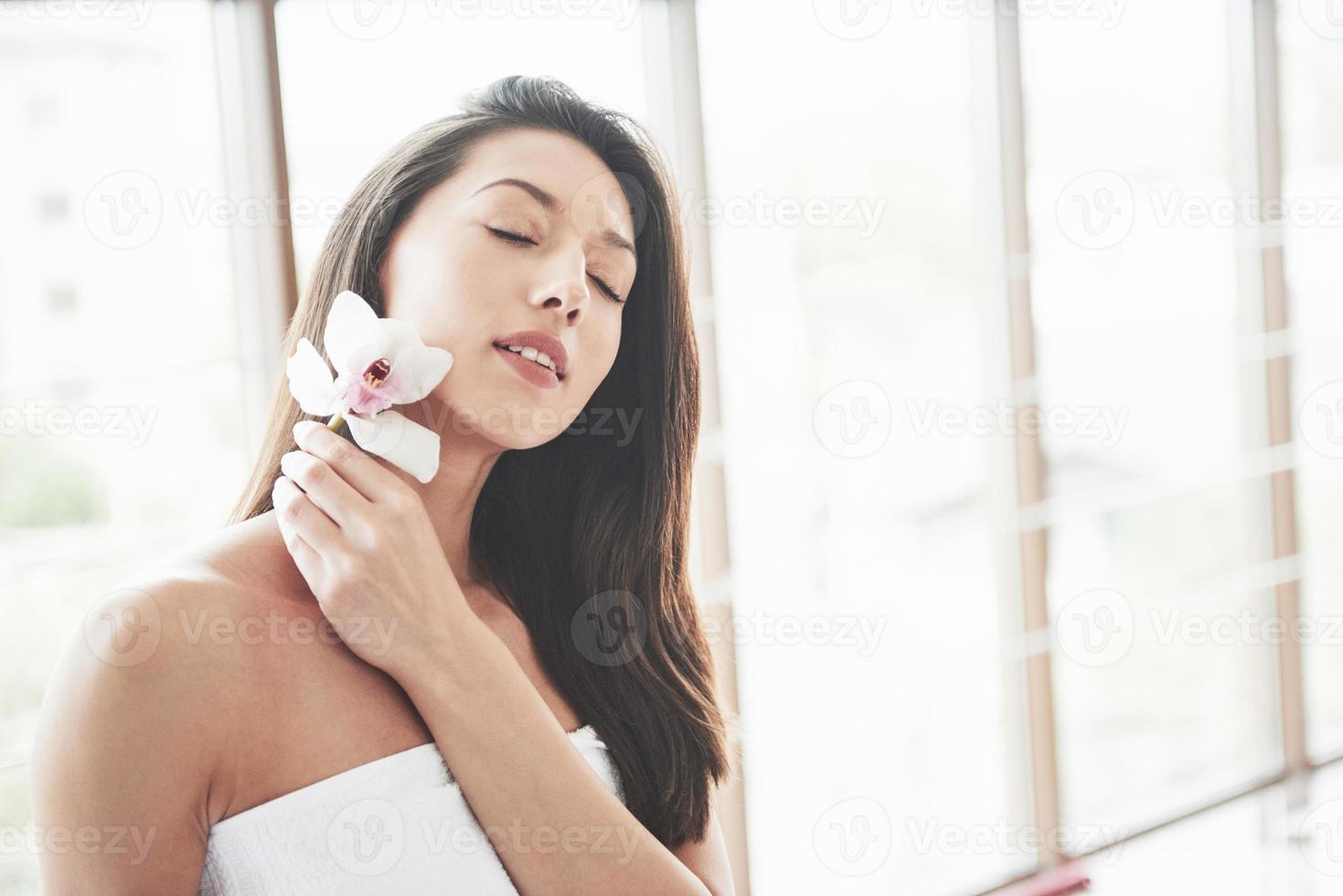 linda garota em uma toalha com uma orquídea, massagem de relaxamento esperando. foto