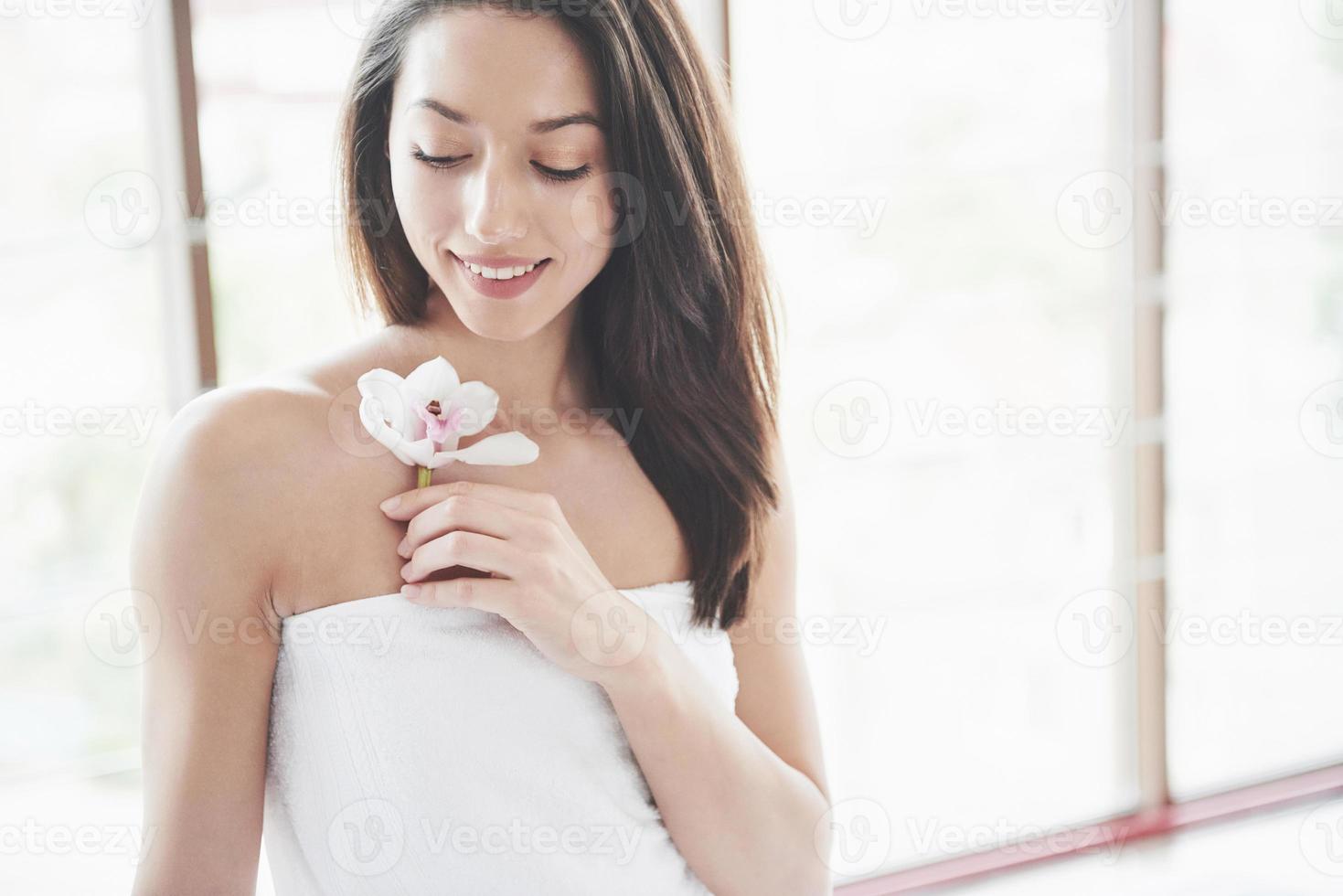 linda garota em uma toalha com uma orquídea, massagem de relaxamento esperando. foto