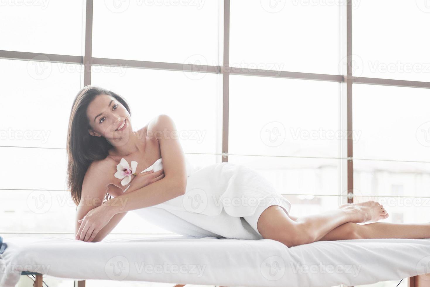 bela jovem relaxando em uma toalha com uma flor de uma orquídea isolada em um fundo branco foto