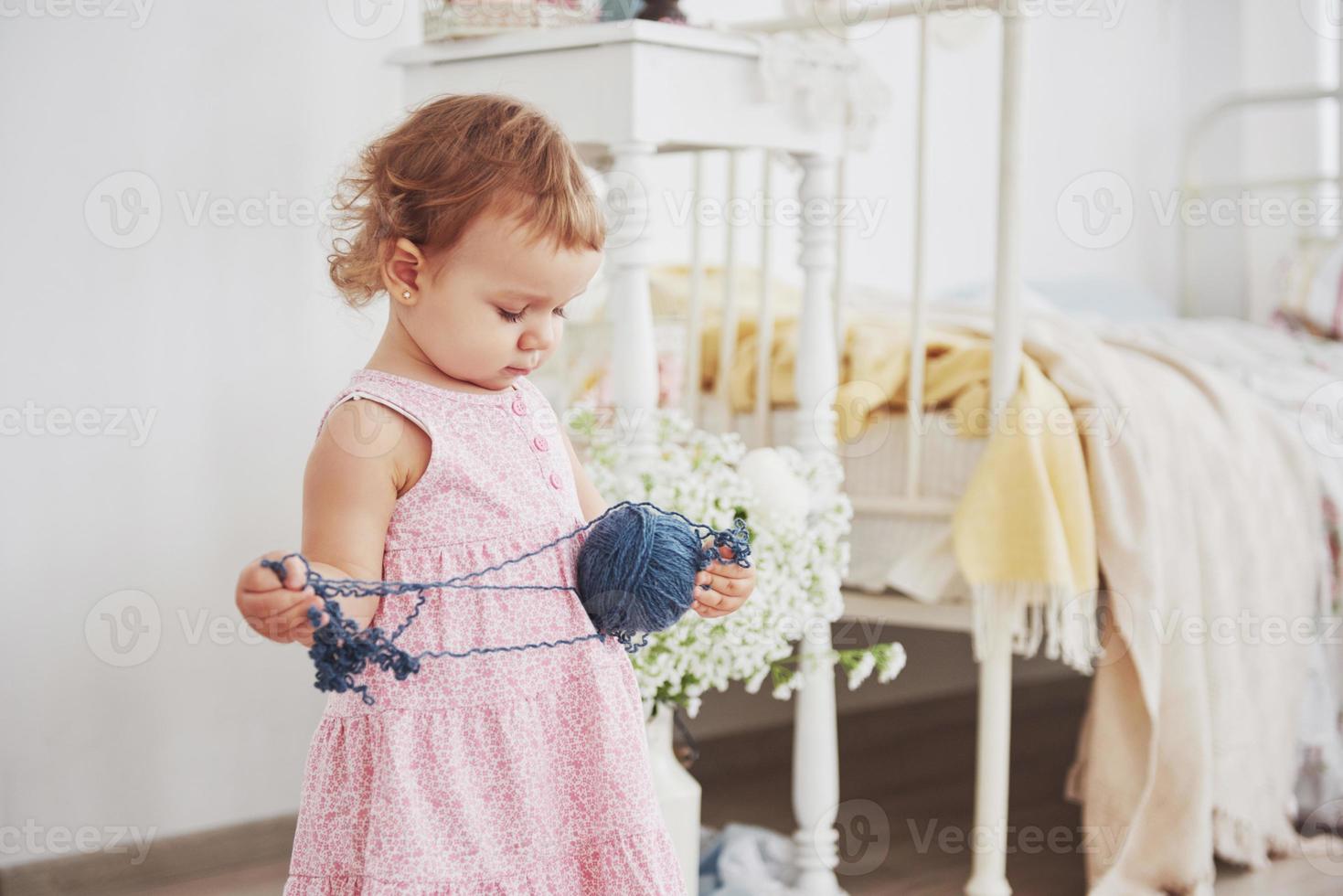 conceito de infância. menina com vestido bonito brincar com fios coloridos. quarto infantil branco vintage foto