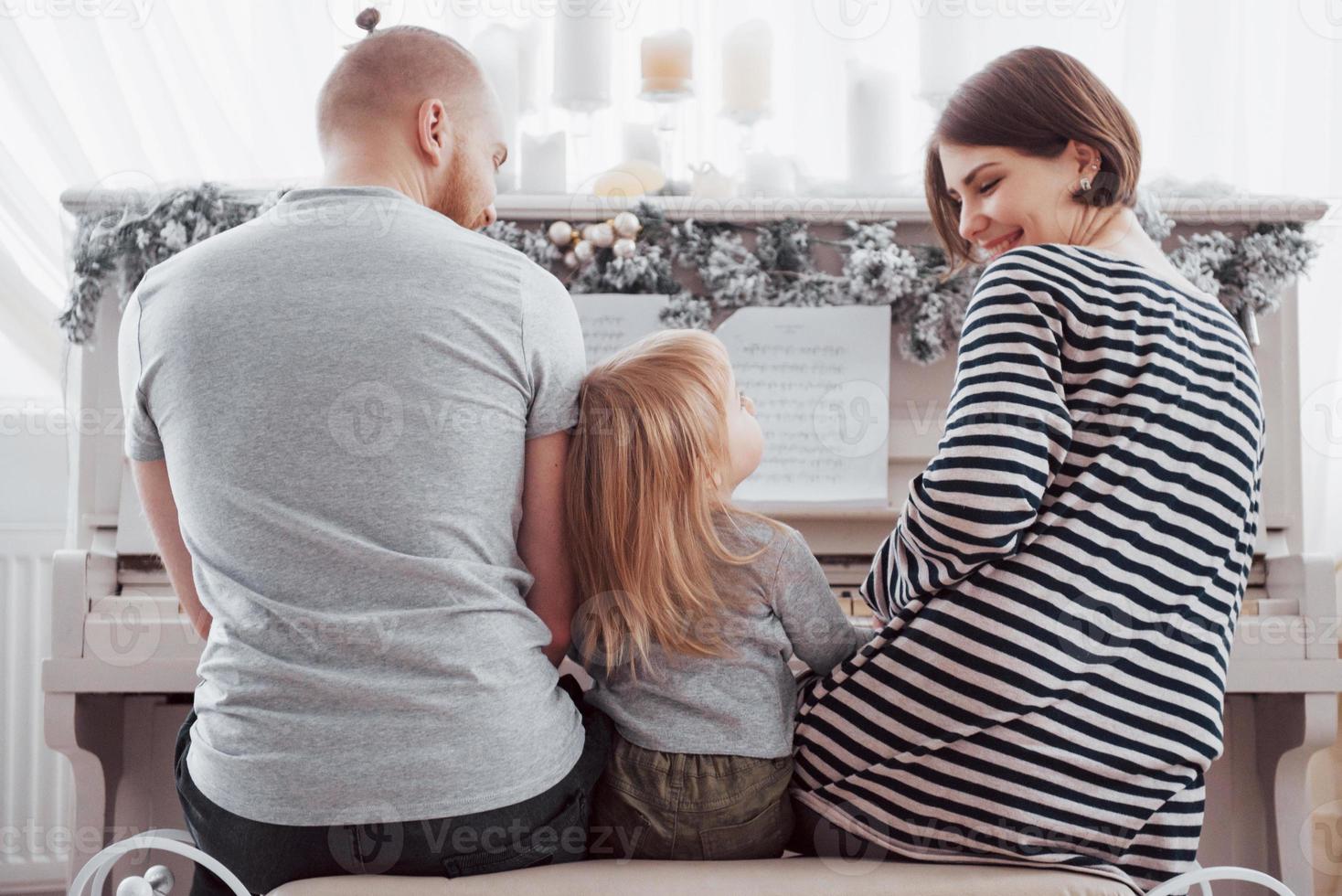 olhe por trás para a mãe, pai e filha tocando piano branco foto