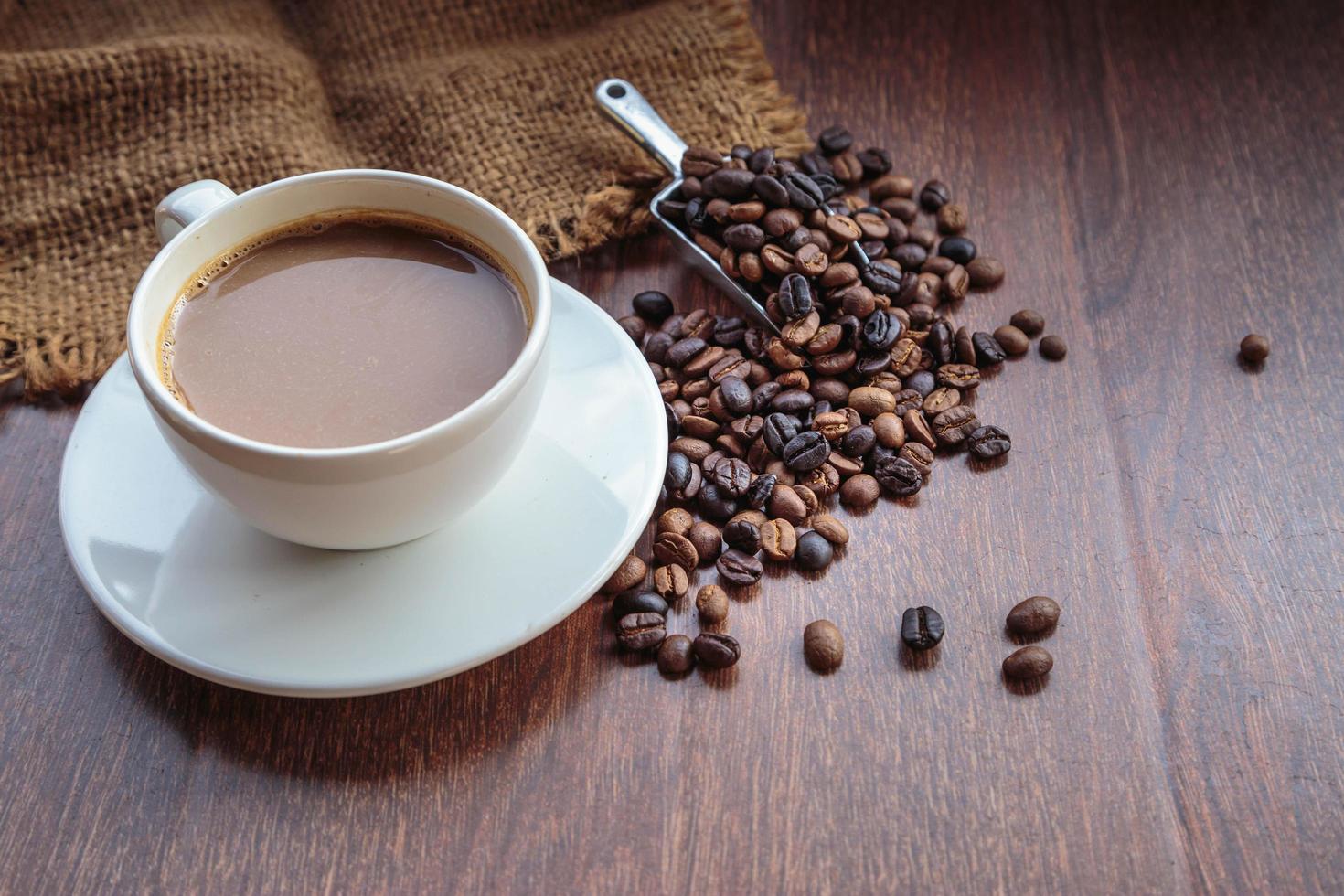 xícara de café e grãos de café em um saco em fundo marrom, vista superior foto