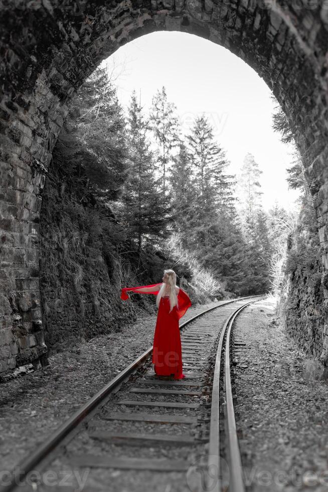 mulher dentro uma vermelho vestir dentro frente do uma estrada de ferro túnel foto