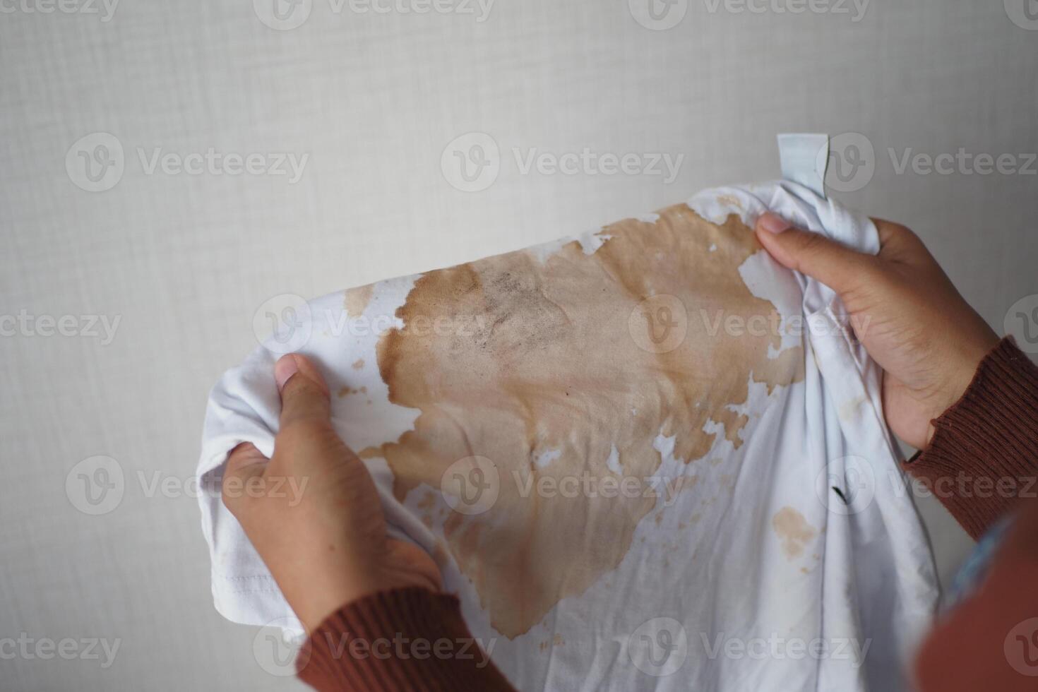 mulheres segurando branco cor sujo camisa, mostrando fazer mancha foto