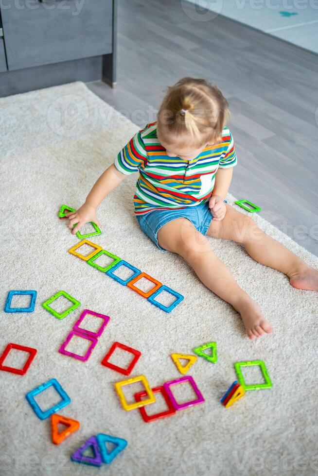 pequeno menina jogando colorida magnético plástico blocos kit às lar. a criança jogando educacional jogos. cedo infância desenvolvimento. foto