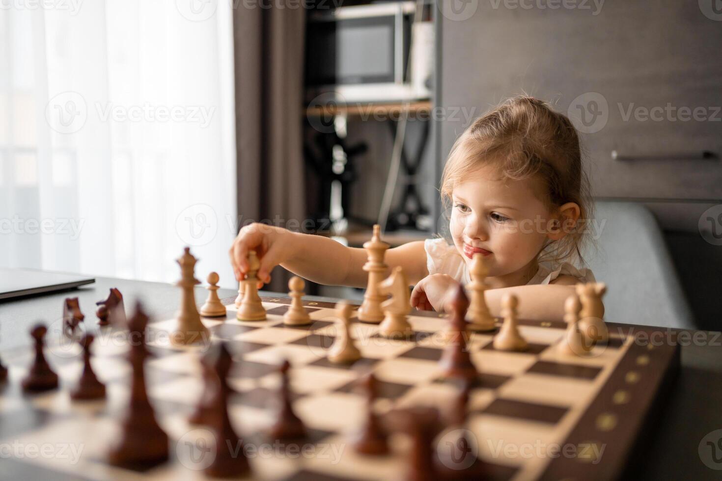 pequeno menina jogando xadrez às a mesa dentro casa cozinha. a conceito cedo infância desenvolvimento e Educação. família lazer, comunicação e lazer. foto