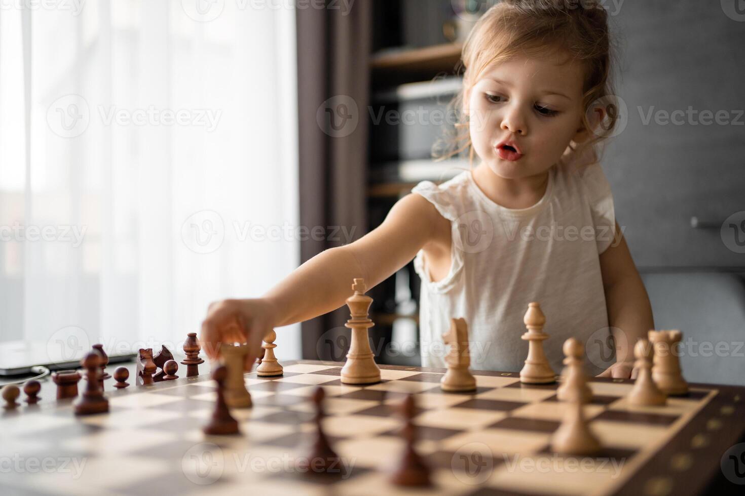 pequeno menina jogando xadrez às a mesa dentro casa cozinha. a conceito cedo infância desenvolvimento e Educação. família lazer, comunicação e lazer. foto