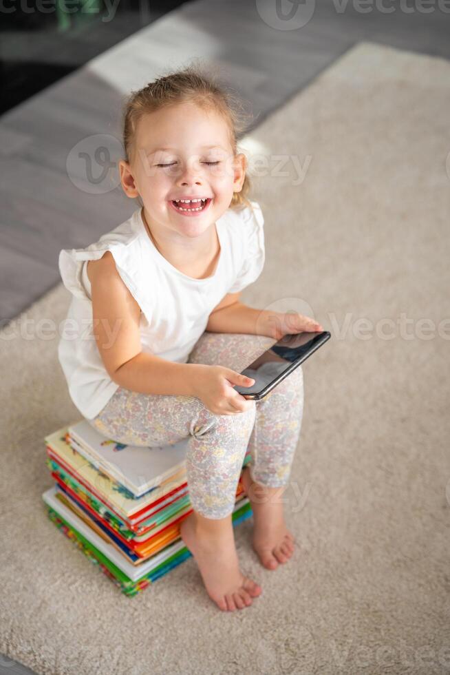 sorridente pequeno menina senta em uma pilha do crianças conto de fadas livros e relógios desenhos animados em dela Smartphone foto