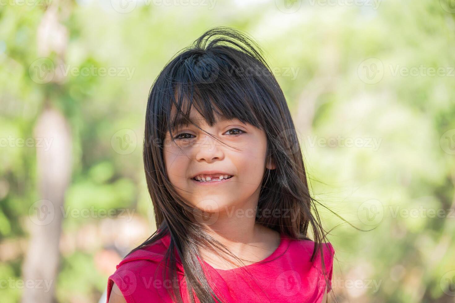 retrato do uma sorridente latim criança olhando às a Câmera com dela cabelo sopro dentro a vento dentro uma parque. foto