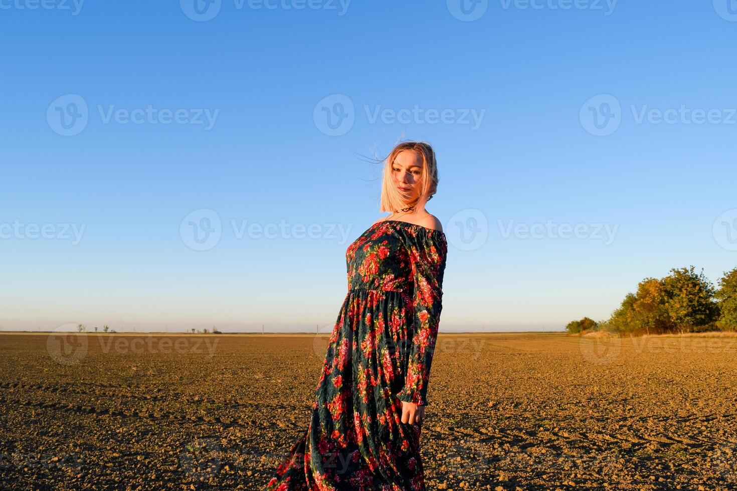 mulher dentro uma arado campo dentro uma vermelho preto vestir em uma pôr do sol fundo. foto