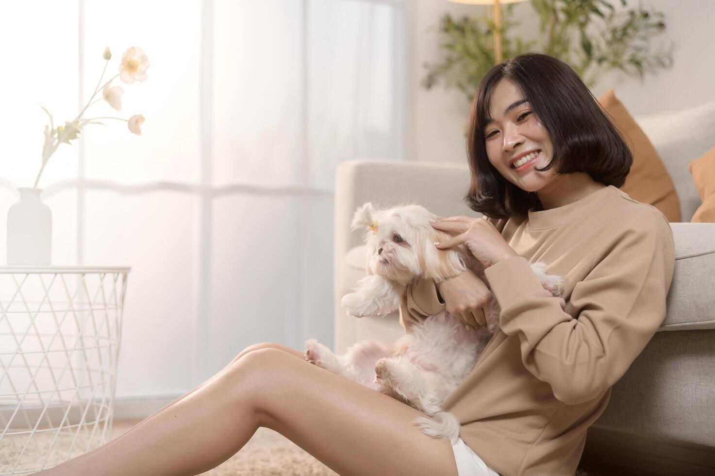 feliz jovem ásia mulher abraço e gastos Tempo com fofa cachorro dentro vivo sala. foto