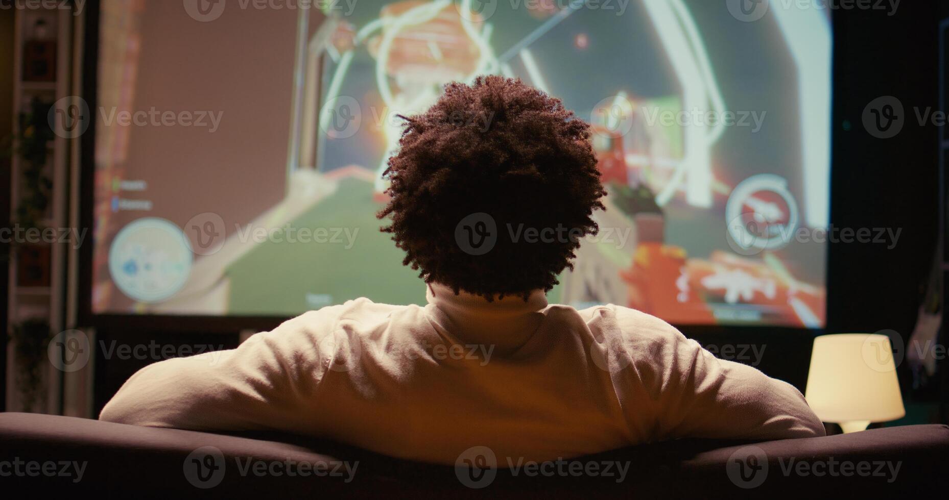 fechar acima tiro do africano americano homem assistindo esports concorrência em gigantesco inteligente televisão, relaxante em sofá. jogador dentro casa teatro Segue jogos torneio em televisão conjunto foto