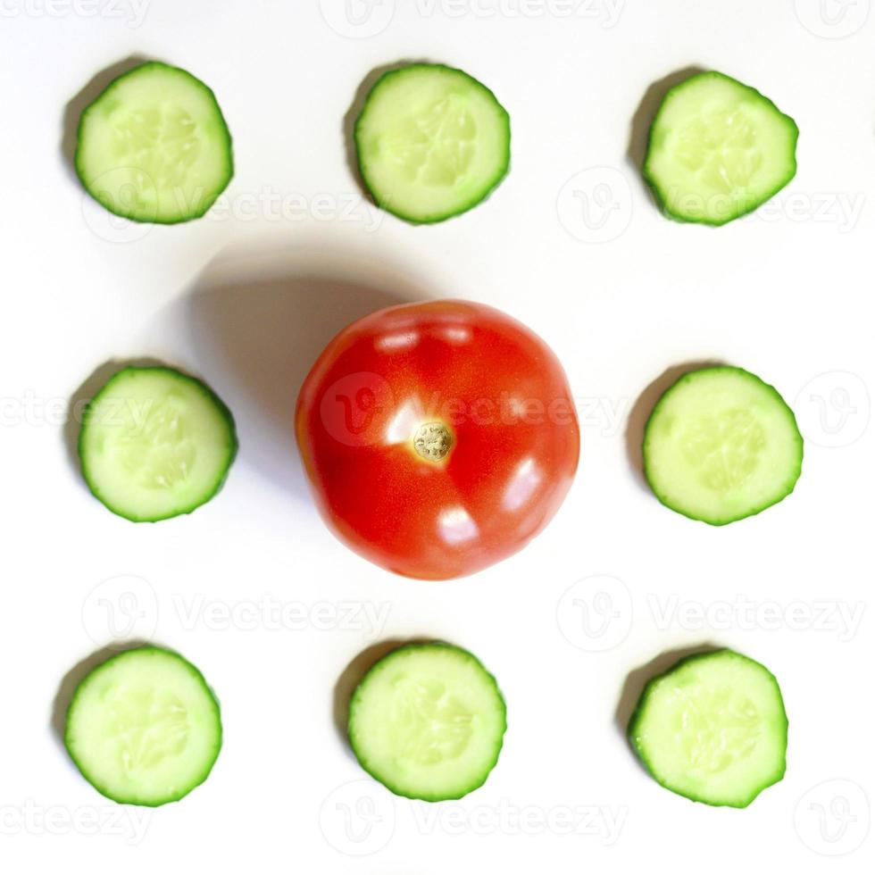 padrão de repetição de semicírculos fatiados de pepinos de vegetais crus frescos para salada e um tomate inteiro foto