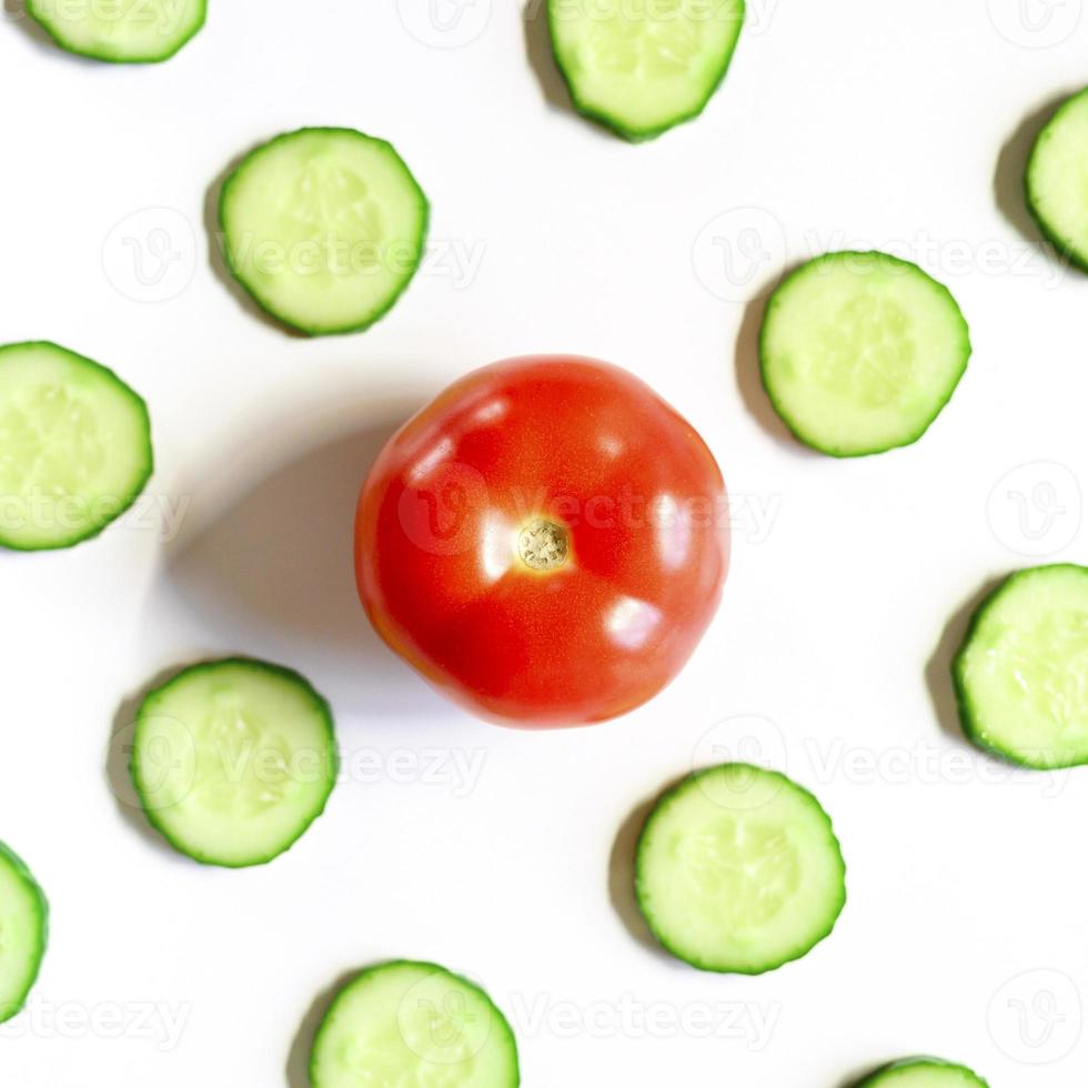 padrão de repetição de semicírculos fatiados de pepinos de vegetais crus frescos para salada e um tomate inteiro foto