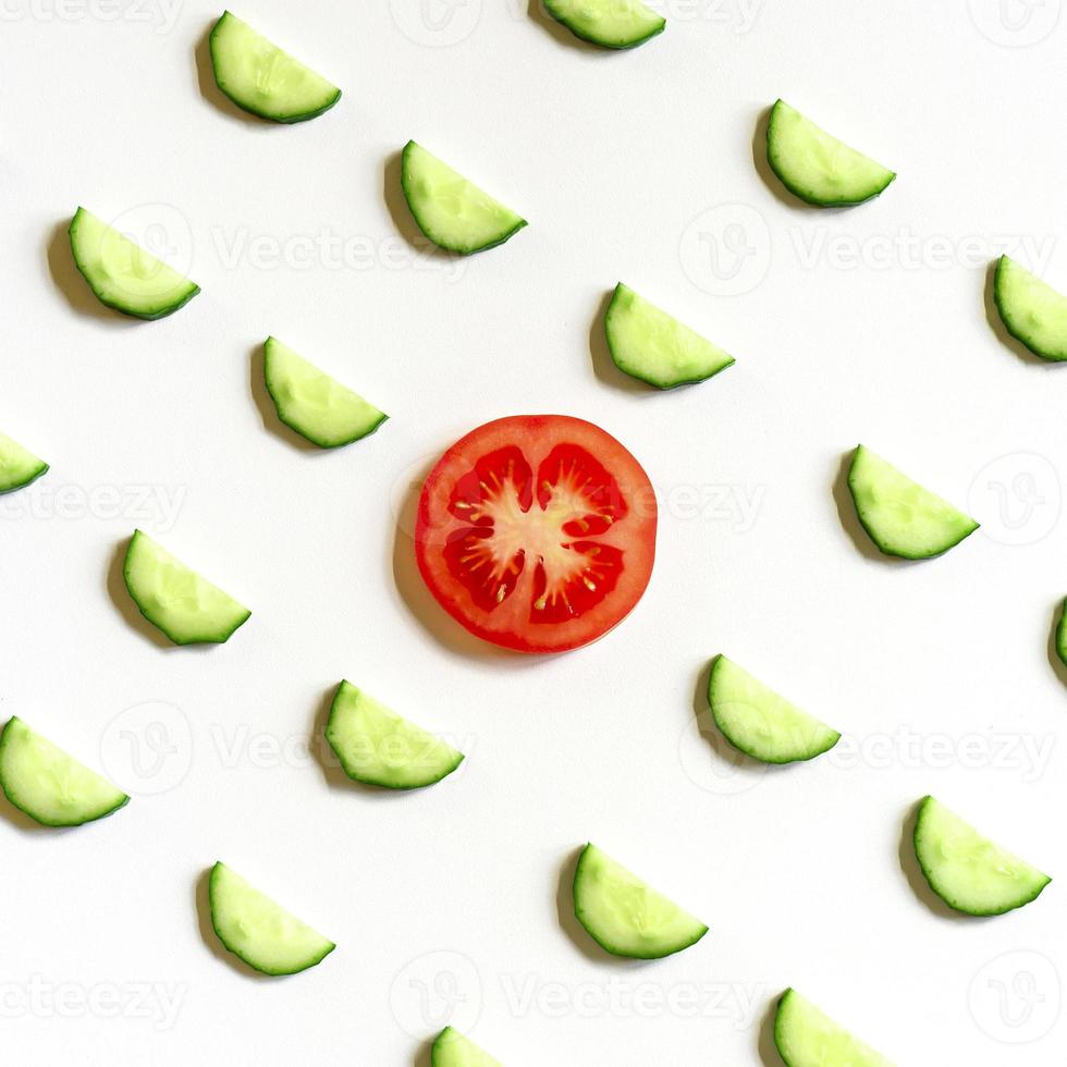 padrão de repetição de semicírculos fatiados de pepinos de vegetais crus frescos para salada e uma fatia de tomate foto
