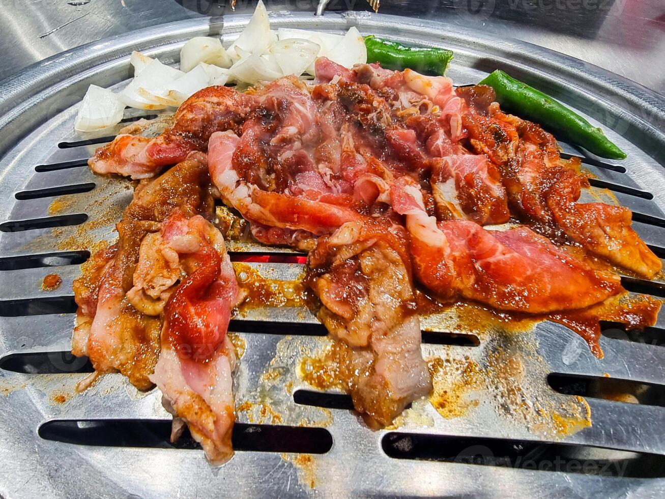 vermelho cru carne de porco fatiado grelhado em churrasco quente frigideira. queimando cebola e vegetal preparação dentro restaurante. pouco saudável Comida Alto óleo cozinhando Comida foto