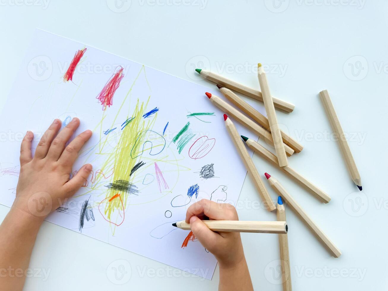 pequeno criança desenha com colori lápis em papel em branco mesa. foto