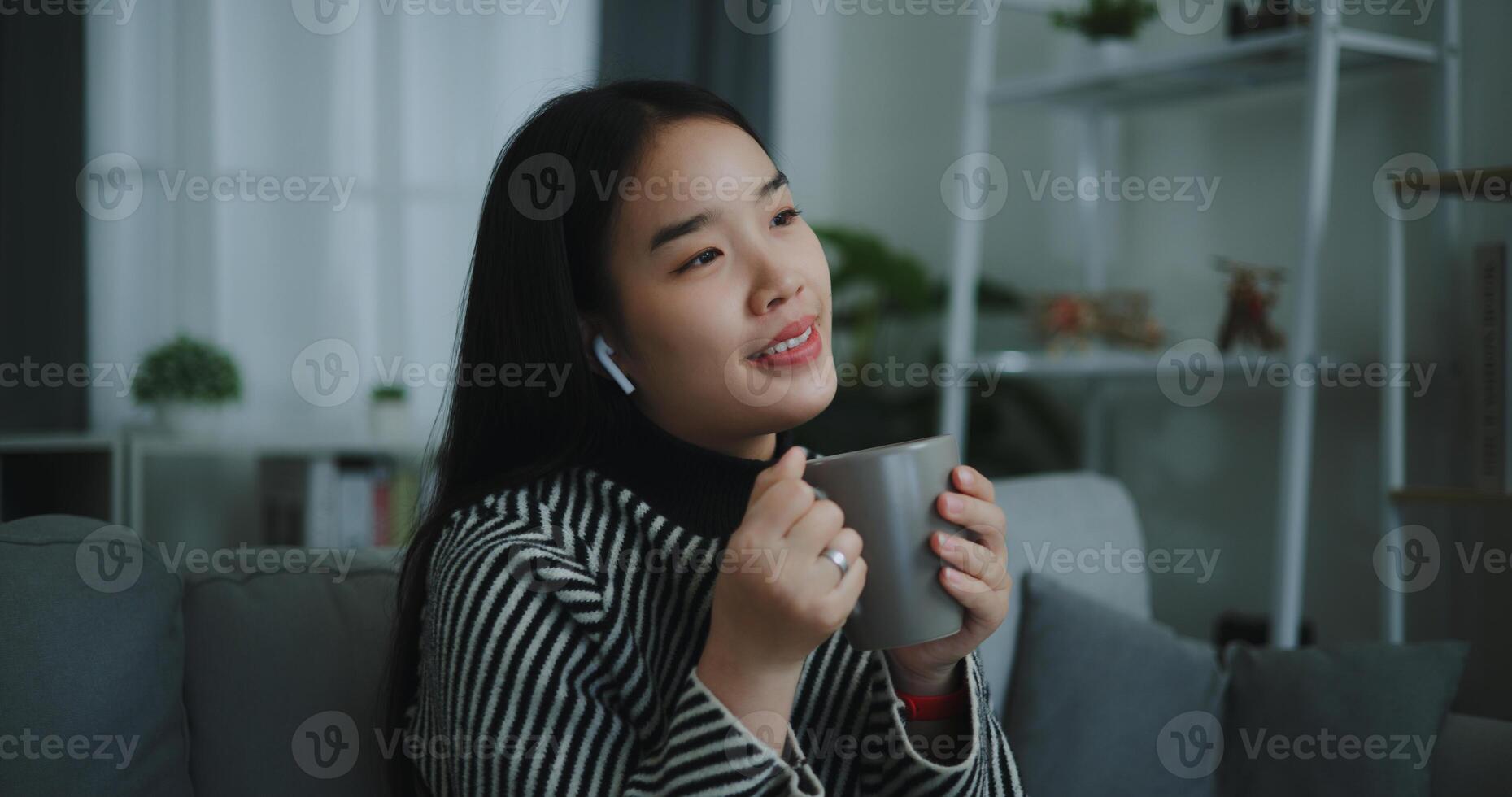 retrato do feliz jovem ásia mulher apreciar ouvindo para a música com sem fio fones de ouvido enquanto sentado beber café em sofá dentro vivo quarto às lar, lazer e estilo de vida, grátis Tempo foto