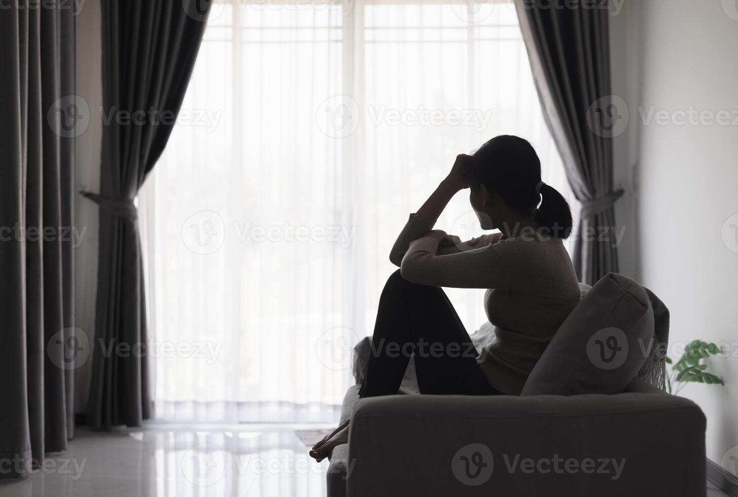 silhueta do uma pessoa sofrimento a partir de depressão dentro a casa, depressivo mulher sentado sozinho em a sofá sentir estresse, triste e preocupado dentro a Sombrio sala. pessoa estão estressado. foto