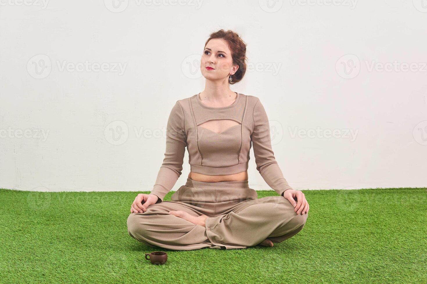 jovem mulher sentado dentro meditação pose e parece acima sonhadoramente em luz fundo foto