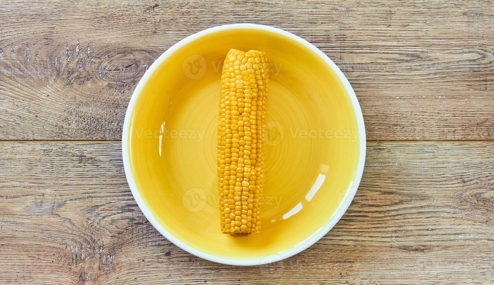 amarelo espiga do fervido milho em uma amarelo prato em uma de madeira de mesa foto