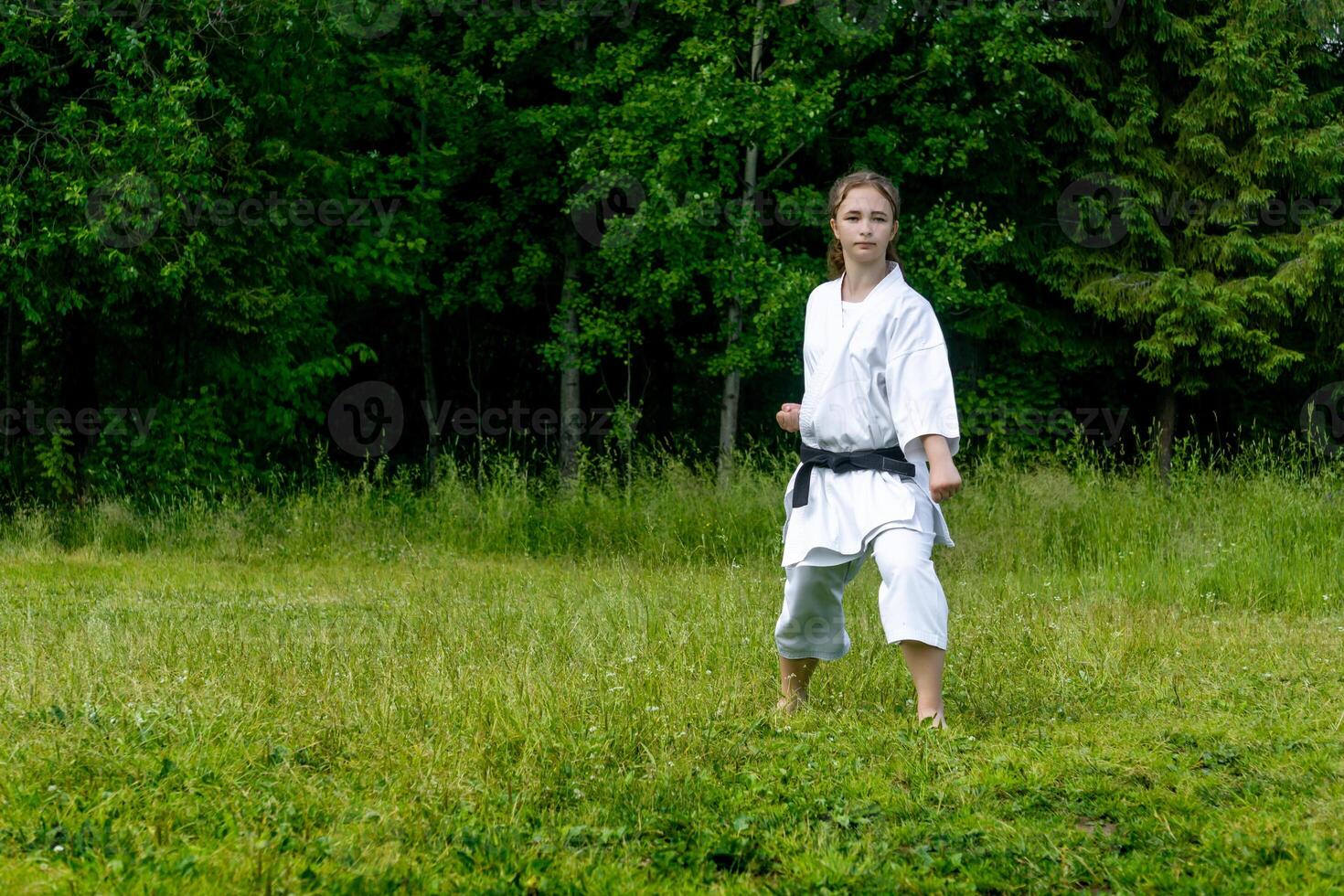 Adolescência menina Treinamento karatê kata ao ar livre, executa gedan-barai para baixo quadra foto