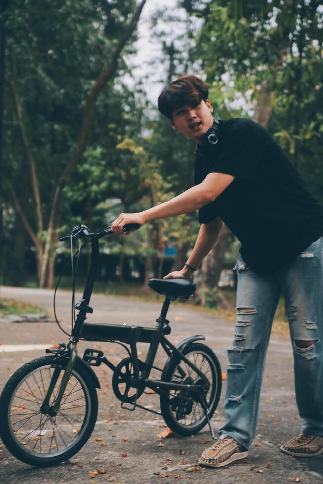 jovem bonito barbudo homem levando uma pausa enquanto viajando a cidade com dele bicicleta usando dele digital tábua olhando longe pensativamente foto