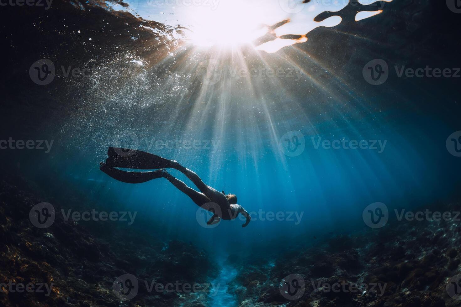 livre mergulhador mulher com barbatanas desliza sobre coral inferior e surpreendente Sol raios. mergulho livre embaixo da agua dentro mar foto