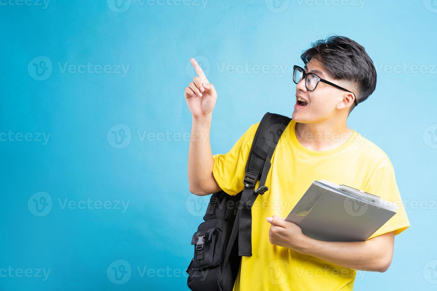 retrato de estudante masculino, isolado em fundo azul, apontando foto