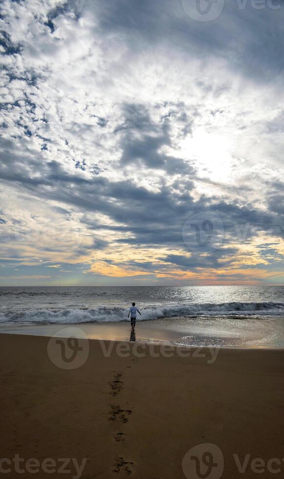jovem homem em a de praia olhando às a pôr do sol, refletindo, espaço para texto foto