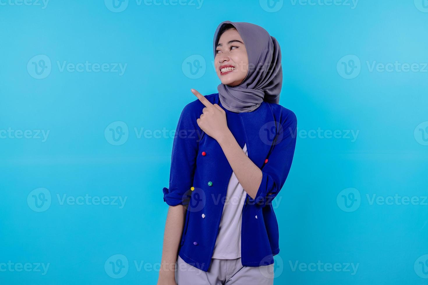 jovem carismática bonita com hijab apontando isolado em fundo azul claro foto