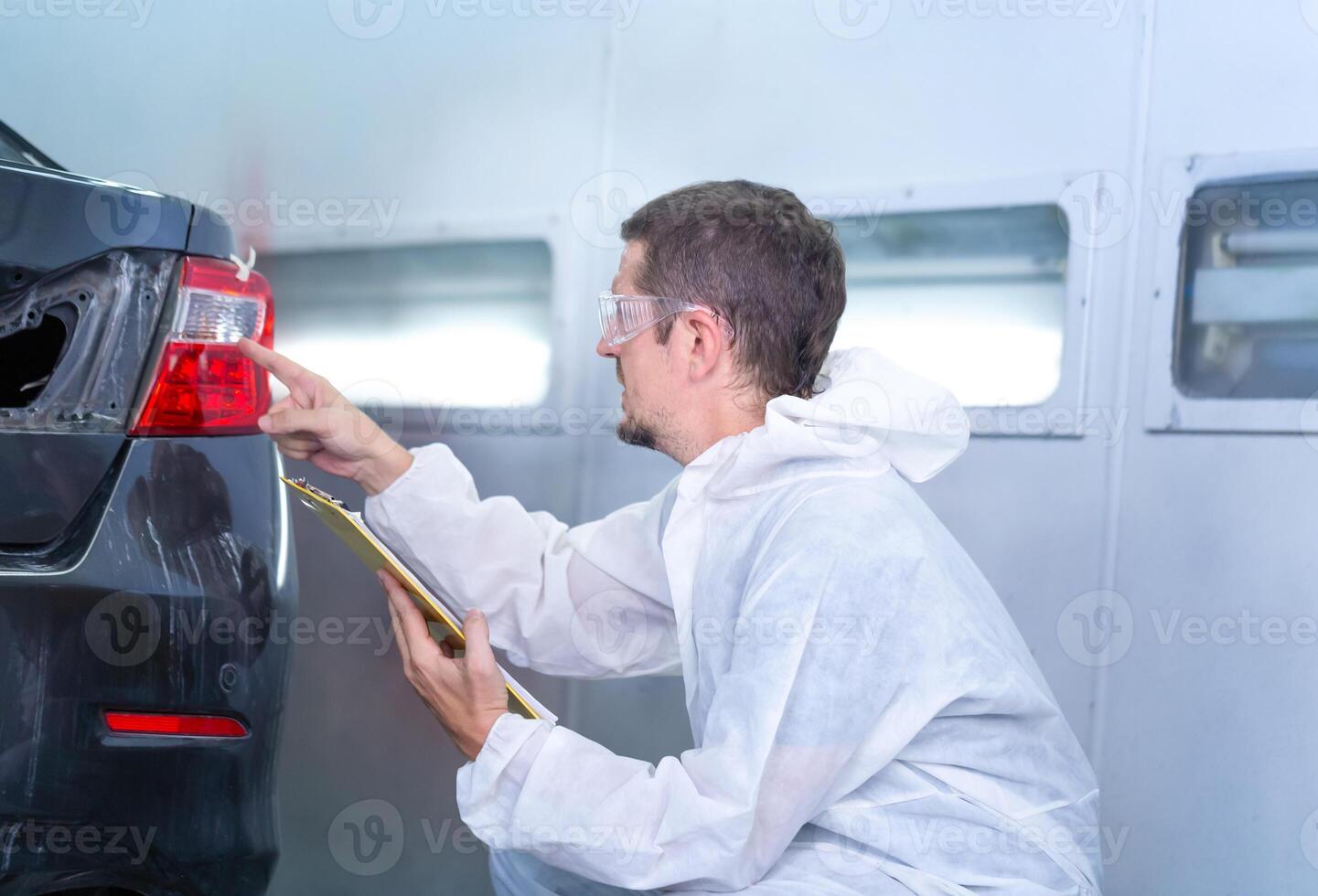 trabalhador homem segurando prancheta lista de controle do a carro às a garagem, mecânico pintura carro dentro a câmara. garagem pintura carro serviço reparar e manutenção foto